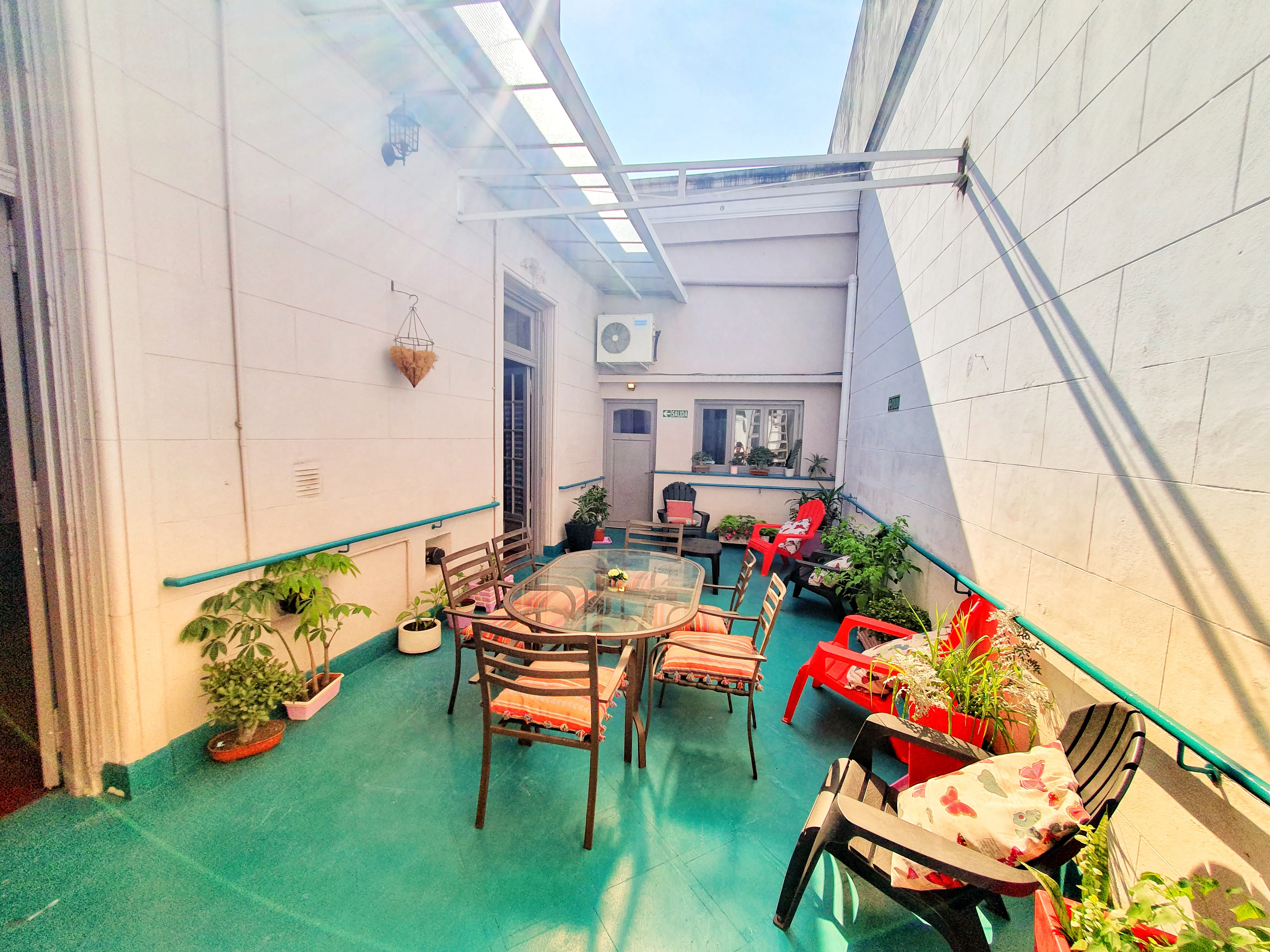 Patio semicubierto con mesa, sillas con almohadones y muchas plantas